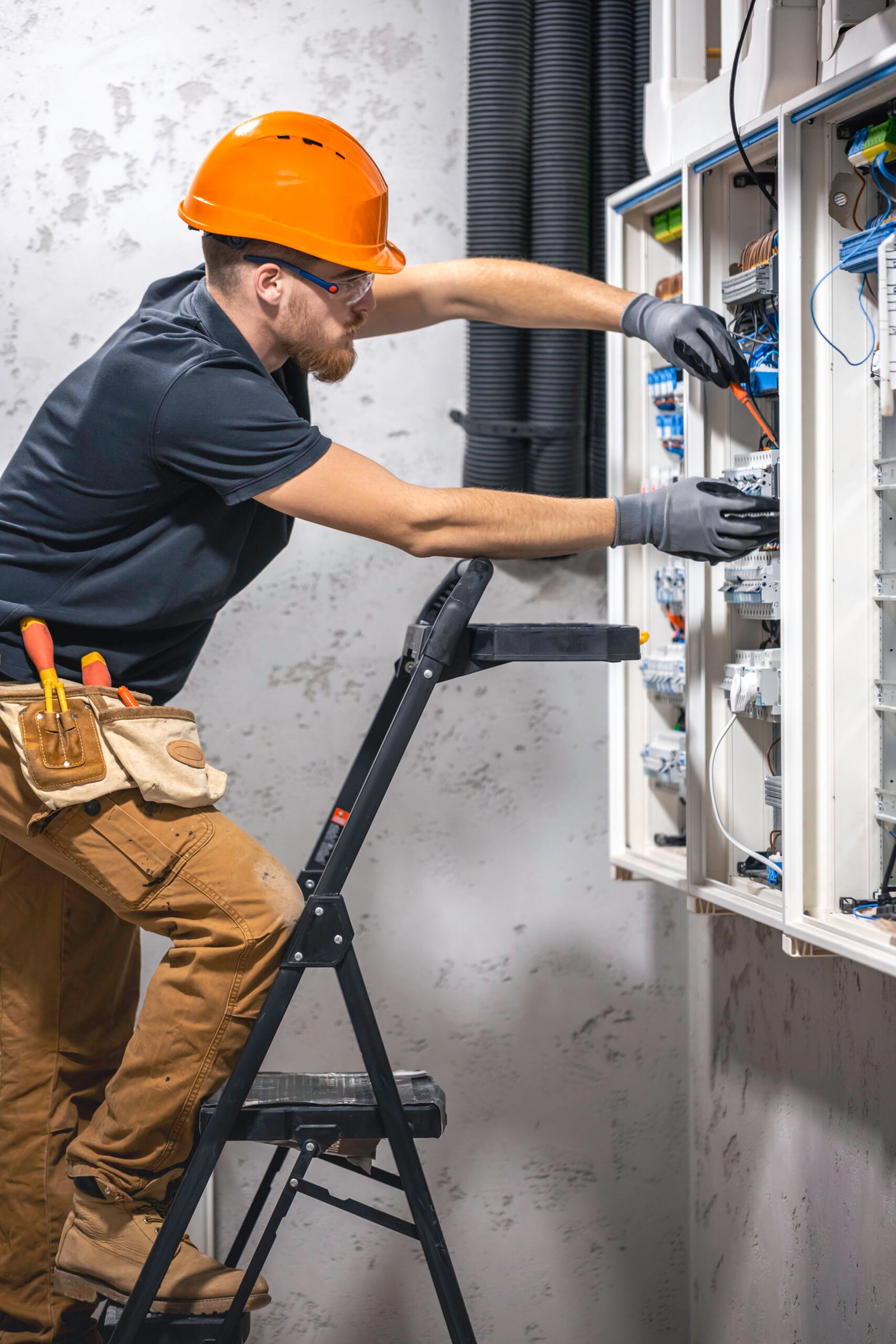 A male electrician works in a switchboard with an electrical connecting cable.